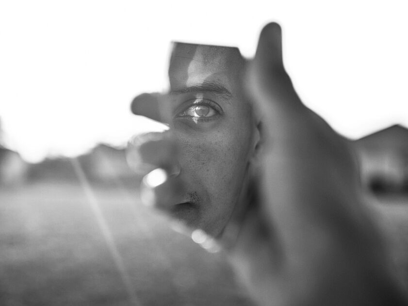 Eine Spiegelscherbe, in der sich das Auge eines Mannes spiegelt. Schwarz-weiß.