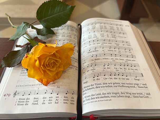 Gelbe Rose liegt auf einem geöffneten Gesangbuch mit Noten und Liedtexten