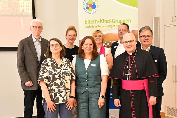 Gruppenfoto von Vertreterinnen und Vertretern der Eltern-Kind-Gruppen gemeinsam mit Bischof Rudolf Voderholzer vor einem Werbebanner