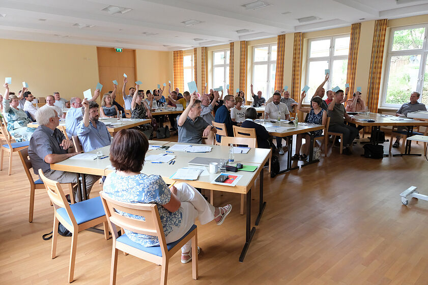 Vertreter der KEB-Mitglieder sitzen in einem großen Saal und stimmen per Handzeichen ab