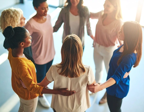 "Mehrere Frauen stehen im Kreis, halten sich an den Schultern und lächeln einander an – ein Symbol für Gemeinschaft, Vertrauen und Austausch."